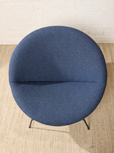Load image into Gallery viewer, Image 4 of 17: A round upholstered lounge chair in textured blue fabric with thin black metal legs, photographed from above on a woven rug against a white brick wall.
