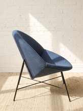Load image into Gallery viewer, Image 5 of 17: A modern blue upholstered accent chair with a black metal frame, set against a white brick wall on a beige woven rug with soft sunlight casting shadows.
