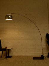 Load image into Gallery viewer, Image 2 of 23: Vintage mid-century modern arc floor lamp featuring a long curved brass-tone metal arm, reflective chrome dome-shaped shade, and heavy black rectangular floor base.
