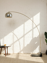 Load image into Gallery viewer, Image 1 of 23: Vintage mid-century modern arc floor lamp featuring a long curved brass-tone metal arm, reflective chrome dome-shaped shade, and heavy black rectangular floor base.
