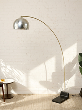 Load image into Gallery viewer, Image 3 of 23: Vintage mid-century modern arc floor lamp featuring a long curved brass-tone metal arm, reflective chrome dome-shaped shade, and heavy black rectangular floor base.

