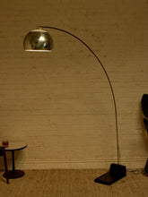 Load image into Gallery viewer, Image 4 of 23: Vintage mid-century modern arc floor lamp featuring a long curved brass-tone metal arm, reflective chrome dome-shaped shade, and heavy black rectangular floor base.
