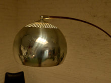 Load image into Gallery viewer, Image 12 of 23: A vintage modernist floor lamp with a large, polished chrome dome shade and a dark brown curved metal arm, set against a warm, off-white brick wall.

