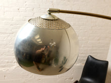 Load image into Gallery viewer, Image 16 of 23: A vintage mid-century modern floor lamp with a polished chrome reflective globe shade and a brass-colored curved arm, shown against a white brick wall.
