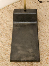 Load image into Gallery viewer, Image 22 of 23: A rectangular black cast iron base with a textured finish and a brass-colored metal rod extending from the top, resting on a beige woven rug.
