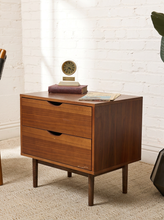 Load image into Gallery viewer, Image 2 of 16: Vintage mid-century modern wooden nightstand featuring two stacked drawers with recessed crescent-shaped pulls, warm walnut-tone wood grain, rectangular cabinet frame, and four slender tapered legs.
