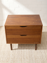 Load image into Gallery viewer, Image 7 of 16: Vintage mid-century modern wooden nightstand featuring two stacked drawers with recessed crescent-shaped pulls, warm walnut-tone wood grain, rectangular cabinet frame, and four slender tapered legs.
