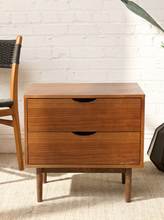 Load image into Gallery viewer, Image 4 of 16: Vintage mid-century modern wooden nightstand featuring two stacked drawers with recessed crescent-shaped pulls, warm walnut-tone wood grain, rectangular cabinet frame, and four slender tapered legs.
