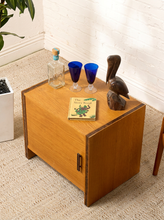 Load image into Gallery viewer, Image 3 of 17: Vintage mid-century modern rectangular wooden cabinet featuring a honey-brown wood grain finish, single flat-panel door, dark vertical metal pull, and contrasting darker wood trim along both sides.
