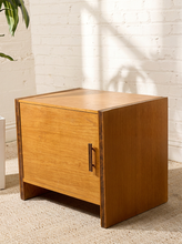 Load image into Gallery viewer, Image 5 of 17: Vintage mid-century modern rectangular wooden cabinet featuring a honey-brown wood grain finish, single flat-panel door, dark vertical metal pull, and contrasting darker wood trim along both sides.
