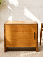 Load image into Gallery viewer, Image 4 of 17: Vintage mid-century modern rectangular wooden cabinet featuring a honey-brown wood grain finish, single flat-panel door, dark vertical metal pull, and contrasting darker wood trim along both sides.
