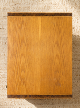 Load image into Gallery viewer, Image 7 of 17: Vintage mid-century modern rectangular wooden cabinet featuring a honey-brown wood grain finish, single flat-panel door, dark vertical metal pull, and contrasting darker wood trim along both sides.
