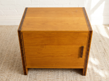 Load image into Gallery viewer, Image 8 of 17: Vintage mid-century modern rectangular wooden cabinet featuring a honey-brown wood grain finish, single flat-panel door, dark vertical metal pull, and contrasting darker wood trim along both sides.
