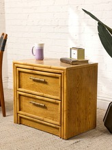 Load image into Gallery viewer, Image 5 of 21: Vintage honey oak nightstand featuring two drawers, natural wood grain, rounded faux-bamboo trim, and antique brass-tone horizontal handles, available as a pair.
