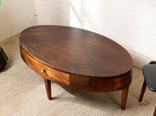 Load image into Gallery viewer, Image 3 of 16: Vintage elongated oval wooden coffee table featuring a dark brown wood finish, gently curved apron, single front storage drawer with a round metal knob, slender tapered legs, and visible surface wear.
