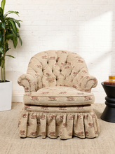 Load image into Gallery viewer, Image 1 of 18: Vintage upholstered barrel chair featuring beige textured fabric with repeating brown lion motifs, a deeply tufted rounded backrest, padded rolled arms, thick seat cushion, and matching ruffled skirt.
