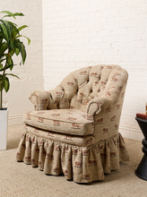 Load image into Gallery viewer, Image 2 of 18: Vintage upholstered barrel chair featuring beige textured fabric with repeating brown lion motifs, a deeply tufted rounded backrest, padded rolled arms, thick seat cushion, and matching ruffled skirt.
