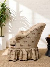 Load image into Gallery viewer, Image 4 of 18: Vintage upholstered barrel chair featuring beige textured fabric with repeating brown lion motifs, a deeply tufted rounded backrest, padded rolled arms, thick seat cushion, and matching ruffled skirt.
