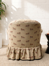 Load image into Gallery viewer, Image 5 of 18: Vintage upholstered barrel chair featuring beige textured fabric with repeating brown lion motifs, a deeply tufted rounded backrest, padded rolled arms, thick seat cushion, and matching ruffled skirt.
