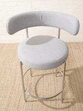 Load image into Gallery viewer, Image 10 of 18: Modern upholstered bar stool featuring a curved beige textured fabric backrest, cushioned seat, slender chrome-finished metal legs, and circular metal footrest. Sold as a pair.
