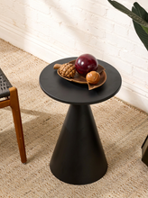 Load image into Gallery viewer, Image 3 of 14: A black round side table with a tapered cone base, styled with a wooden bowl of decorative fruit on a beige woven rug against a white brick wall.
