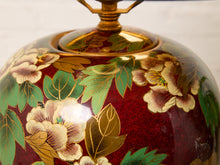 Load image into Gallery viewer, Image 13 of 19: Close-up of a decorative ceramic vase or lantern with a glossy deep red body, hand-painted floral motifs in cream, green, and gold, and a gold-toned metal finial at the top.
