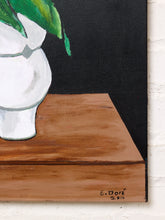 Load image into Gallery viewer, Image 7 of 8: A close-up of a painted still life showing a white vase with green leaves on a brown wooden surface against a black background, mounted on a white brick wall.
