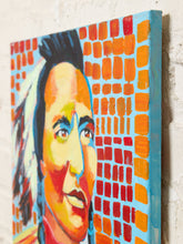 Load image into Gallery viewer, Image 6 of 8: A close-up of a colorful painted canvas showing part of a portrait with bright orange, red, yellow, blue, and black brushstrokes, photographed against a light textured wall.

