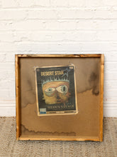 Load image into Gallery viewer, Image 8 of 8: A rustic, handcrafted wooden frame with a brown water-stained backing board, holding a vintage-style 'Desert Star' concert poster for Shawn Savage, set against a white brick wall and textured rug.
