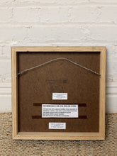 Load image into Gallery viewer, Image 9 of 9: The back of a framed art work by Thomas Hartley, featuring a light natural wood frame, brown backing board, hanging wire, and printed conservation labels, set against a white brick wall and woven rug.
