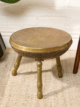 Load image into Gallery viewer, Image 1 of 13: Vintage round brass-tone foot warmer featuring a circular top with intricate floral and scrollwork engravings, a raised rounded rim, warm aged patina, and three short turned metal legs.
