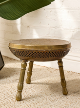 Load image into Gallery viewer, Image 2 of 13: Vintage round brass-tone foot warmer featuring a circular top with intricate floral and scrollwork engravings, a raised rounded rim, warm aged patina, and three short turned metal legs.
