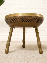 Load image into Gallery viewer, Image 5 of 13: Vintage round brass-tone foot warmer featuring a circular top with intricate floral and scrollwork engravings, a raised rounded rim, warm aged patina, and three short turned metal legs.
