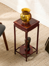 Load image into Gallery viewer, Image 3 of 16: A small square wooden side table with a dark reddish-brown finish, styled with a yellow ceramic pitcher on top and a dark sculpture on the lower shelf, set on a woven jute rug.
