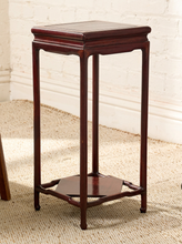 Load image into Gallery viewer, Image 5 of 16: A dark reddish-brown wooden side table with a square top, four slender legs, and an open lower shelf, shown in a room setting on a woven rug against a white brick wall.
