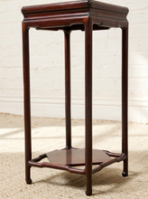 Load image into Gallery viewer, Image 12 of 16: A dark reddish-brown wooden stand or pedestal with four legs and a lower shelf, photographed indoors against a light brick wall and woven rug.
