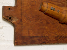 Load image into Gallery viewer, Image 5 of 9: A close-up of a rustic wooden board or plaque with a curved cutout and visible wood grain, alongside a small cylindrical wooden object marked 'DOC'.
