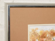 Load image into Gallery viewer, Image 4 of 8: Close-up of a framed art print showing a tan mat board, a silver metallic frame edge, and part of a watercolor painting with warm orange and yellow tones.
