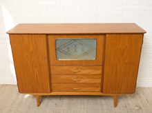 Load image into Gallery viewer, Image 5 of 27: A mid-century modern wooden sideboard cabinet with a warm honey-toned wood finish, featuring two side cabinets, three drawers in the center, and a decorative glass panel above the drawers.
