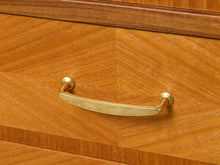 Load image into Gallery viewer, Image 14 of 27: A close-up of a curved brass drawer pull handle mounted on a warm wood-grain cabinet door.
