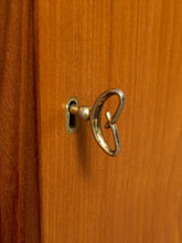 Load image into Gallery viewer, Image 19 of 27: A close-up of a brass door knob with a decorative interlocking ring design, mounted on a warm brown wooden door.
