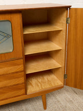 Load image into Gallery viewer, Image 26 of 27: A mid-century modern wooden sideboard cabinet with its door open, showing four interior shelves. The cabinet features a warm honey-toned wood finish, a geometric patterned drawer front, and a glass-front upper section on the left.
