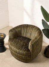 Load image into Gallery viewer, Image 2 of 16: Rowan Swivel Chair in Kenai Olive featuring olive, mustard, and charcoal abstract linear patterned upholstery, a rounded barrel backrest, curved arms, a generously cushioned seat, and a low-profile circular swivel base.
