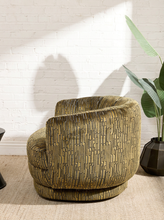 Load image into Gallery viewer, Image 4 of 16: A modern barrel-style armchair with a textured, vertically striped woven pattern in olive green and beige, set in a room with a white brick wall, natural light shadows, and a potted plant.
