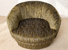 Load image into Gallery viewer, Image 7 of 16: A modern barrel-style armchair upholstered in textured vertical-striped fabric with a metallic gold and black pattern, set on a beige rug against a white brick wall.
