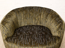 Load image into Gallery viewer, Image 8 of 16: A close-up of a modern barrel-style armchair upholstered in a textured fabric with a vertical linear pattern in olive green, gold, and black.
