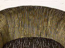 Load image into Gallery viewer, Image 10 of 16: Close-up of a curved upholstered chair back with a textured geometric pattern in olive green, black, and white, set against a white brick wall background.
