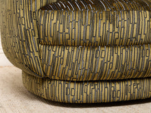 Load image into Gallery viewer, Image 14 of 16: Close-up of a modern upholstered chair or ottoman with a geometric patterned fabric in olive green and black, resting on a light beige textured rug.
