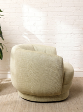 Load image into Gallery viewer, Image 4 of 16: A modern barrel-style armchair upholstered in a textured cream-beige bouclé fabric, set against a white brick wall on a woven rug.
