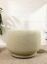 Load image into Gallery viewer, Image 5 of 16: A modern round upholstered accent chair in a textured light beige fabric, set against a white brick wall on a woven rug.
